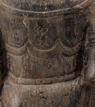 An archaistic stone sculpture of a deity, with characters to the back.