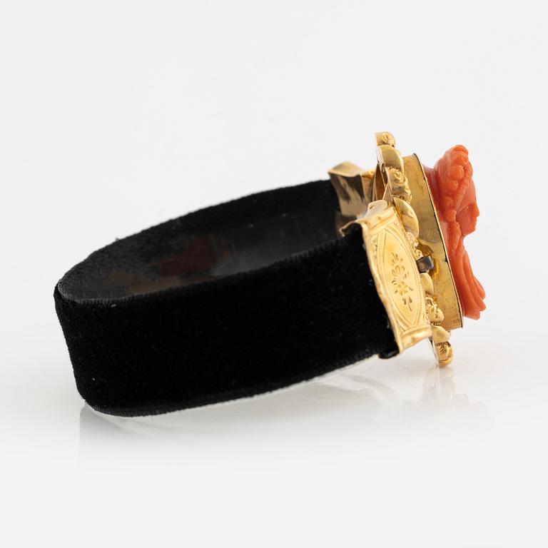 An 18K gold and coral cameo braclet with a black band.
