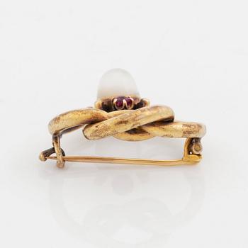 A 14K gold brooch set with a cabochon-cut moonstone and a pink sapphire.