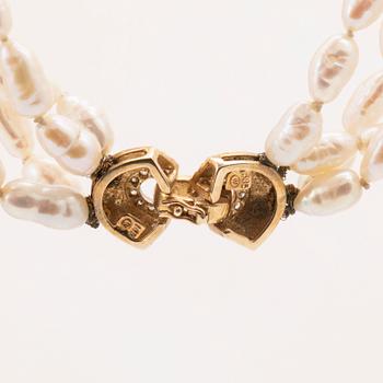 A necklace of cultured pearls set with a 14K gold lock and round brilliant cut diamonds.