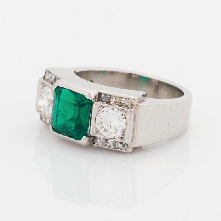 A platinum ring set with a step-cut emerald and round brilliant- and step-cut diamonds.