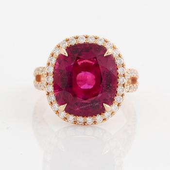 An 18K gold ring set with a faceted pink tourmaline and round brilliant-cut diamonds.
