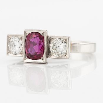 A platinum ring with a faceted ruby and two round brilliant-cut diamonds.