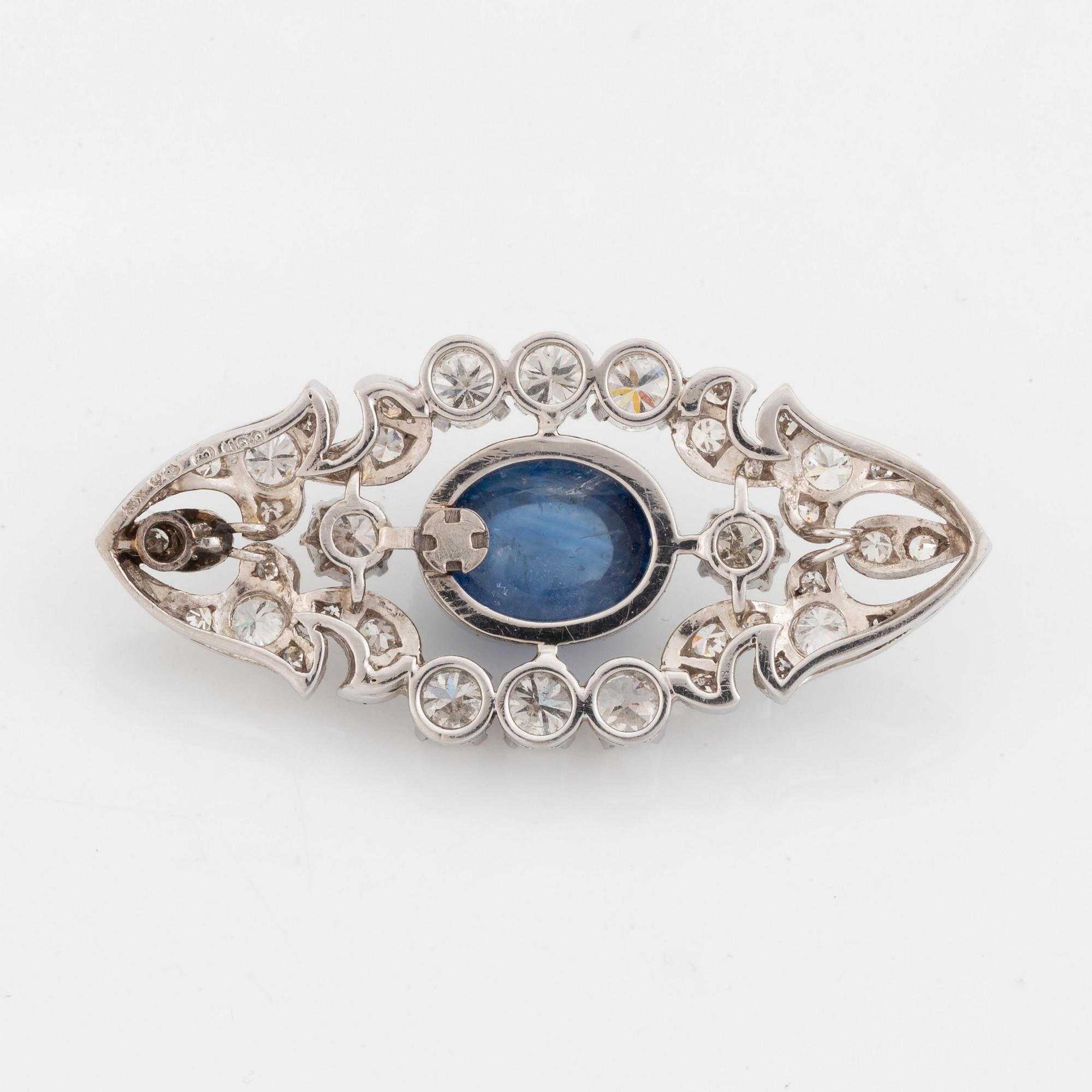 A platinum brooch set with a cabochon-cut sapphire and a cabochon-cut emerald.