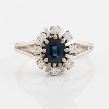 An 18K white gold ring set with a faceted sapphire and round brilliant-cut diamonds.