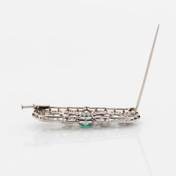 A platinum brooch set with a step-cut emerald and old- and eight-cut diamonds.