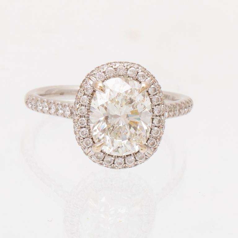 An 18K white gold ring by James Allen, set with an oval brilliant cut diamond in a halo of round brilliant cut diamonds.
