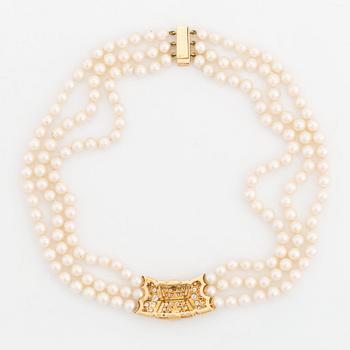 A Cartier triple strand cultured pearl necklace with an 18K gold clasp set with round brilliant-cut diamonds.