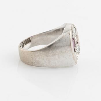 An 18K white gold ring set with a faceted ruby and round brilliant-cut diamonds.