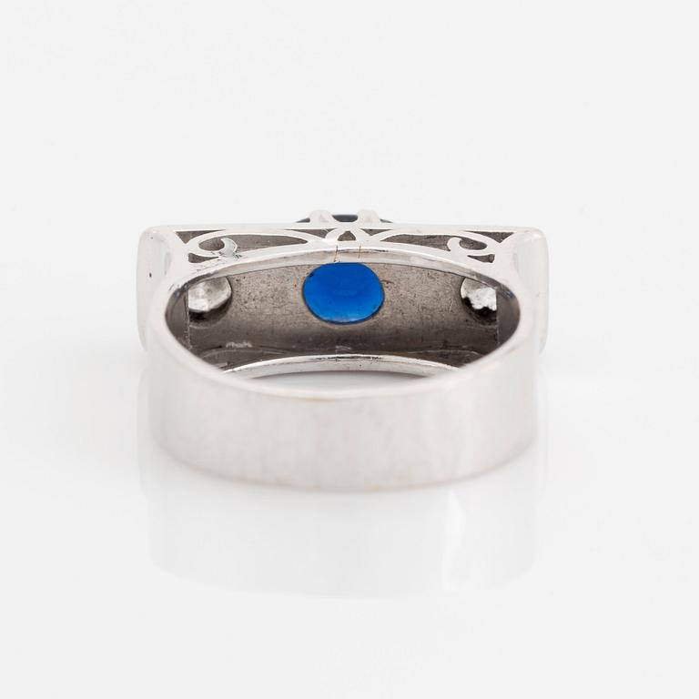An 18K white gold ring set with a faceted sapphire, possibly synthetic, and round brilliant-cut diamonds.