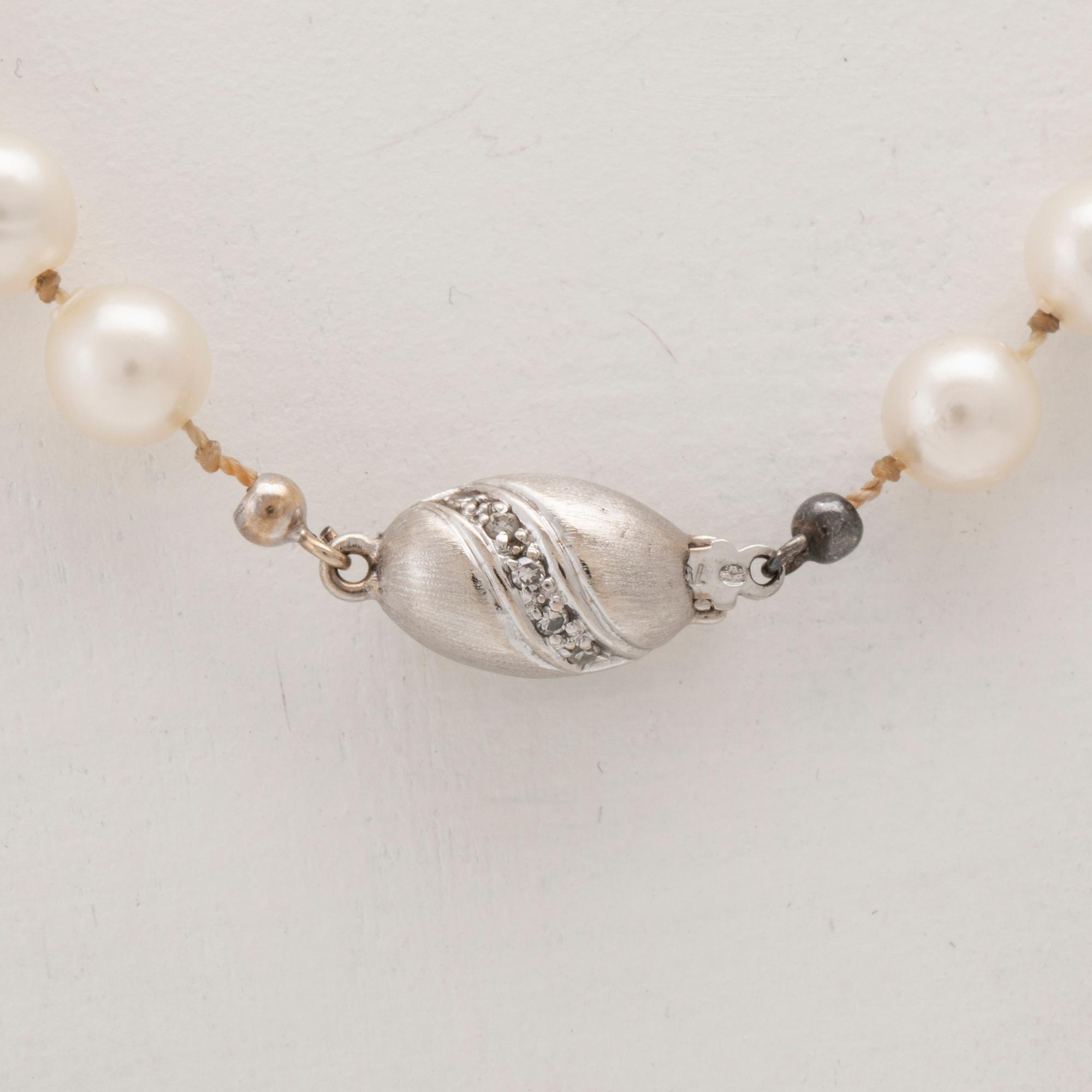 A necklace of cultured pearls with an 18K white gold lock set with single cut diamonds.