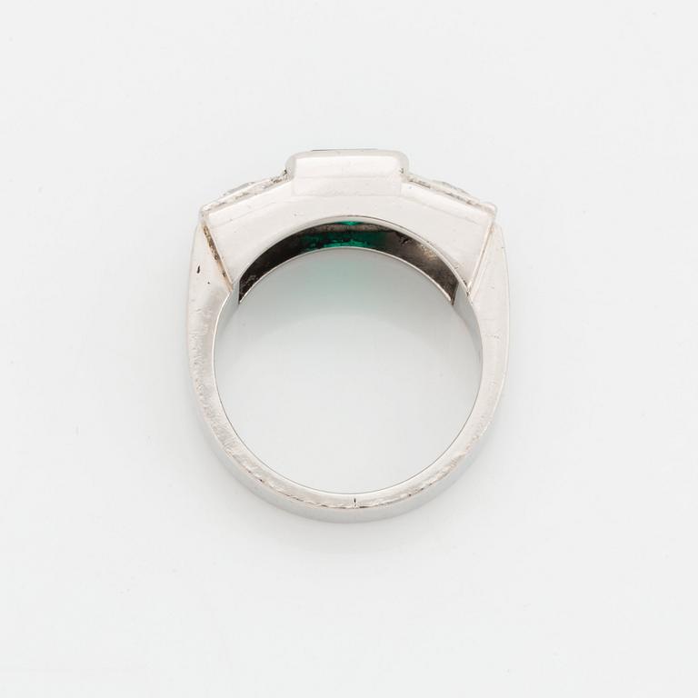 A platinum ring set with a step-cut emerald and round brilliant- and step-cut diamonds.