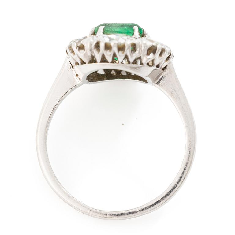 18K white gold ring set with a faceted emerald and round brilliant-cut diamonds.