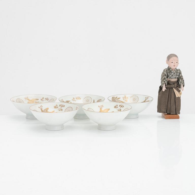 Five porcelain sake cups and a papier maché doll, Japan first half of the 20th century.