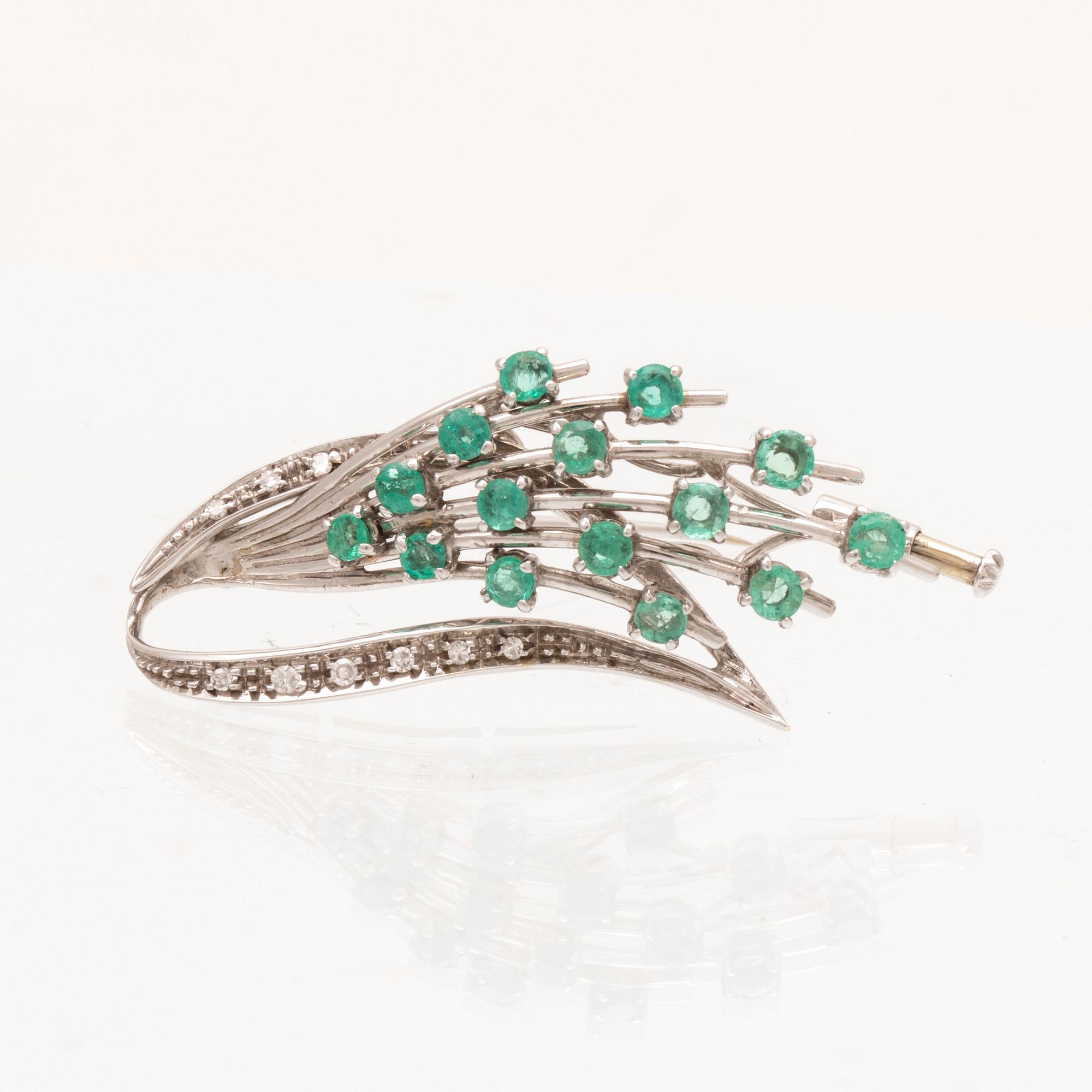 An 18K white gold brooch with round brilliant cut emeralds and single cut diamonds.
