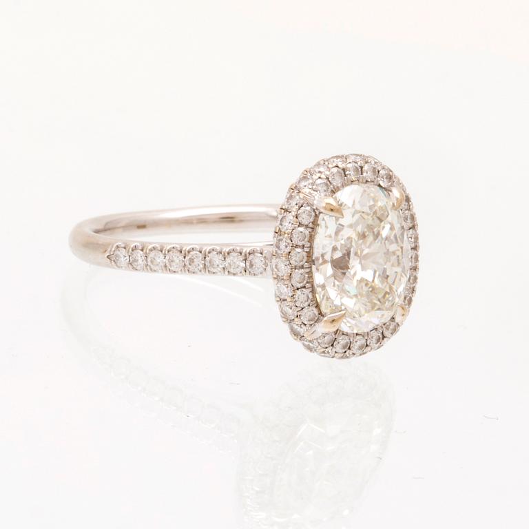 An 18K white gold ring by James Allen, set with an oval brilliant cut diamond in a halo of round brilliant cut diamonds.