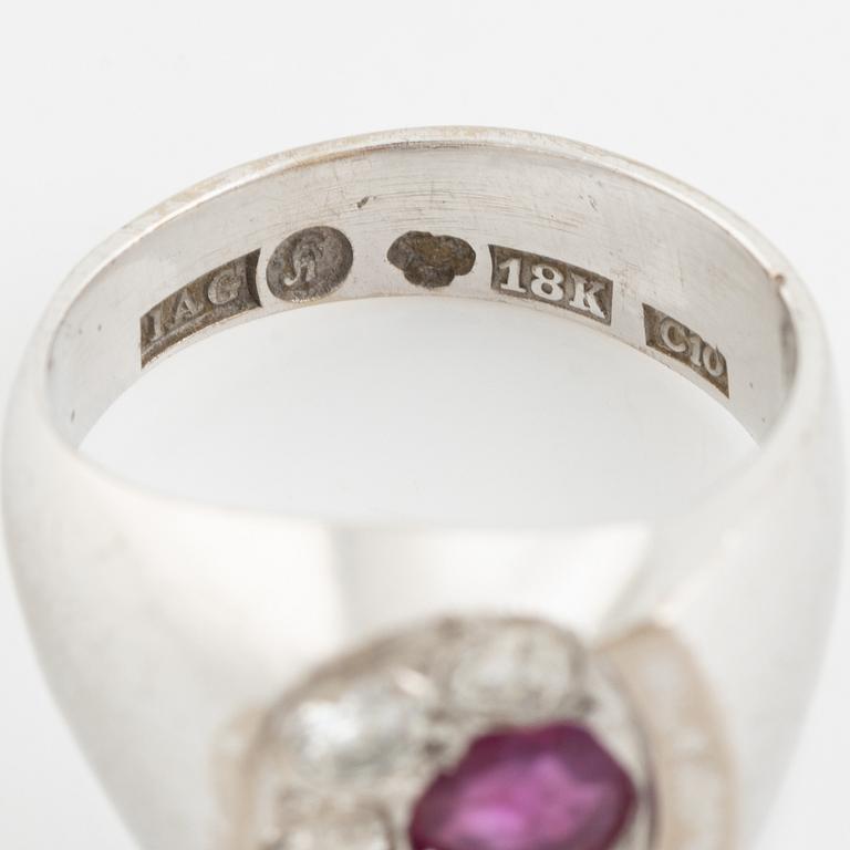 An 18K white gold ring set with a faceted ruby and round brilliant-cut diamonds.