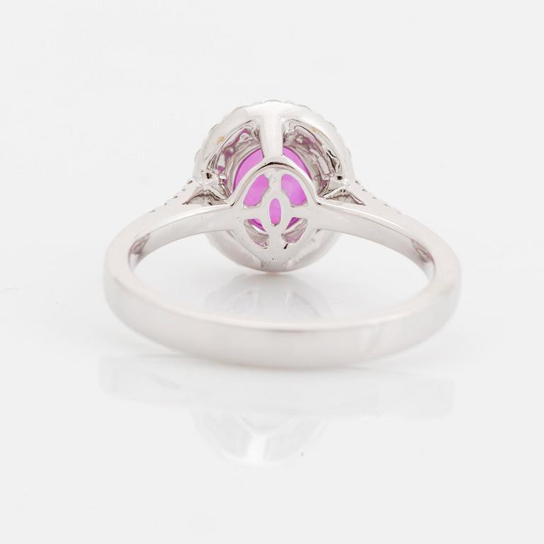 An 18K white gold ring set with a faceted pink sapphire and round brilliant-cut diamonds.