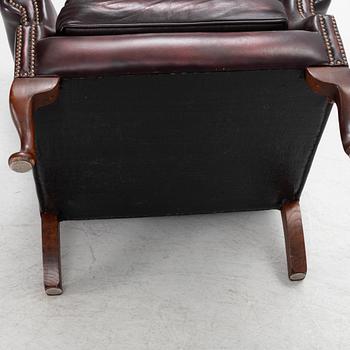 A leather upholstered wingback chair with stool. end of the 20th Century.