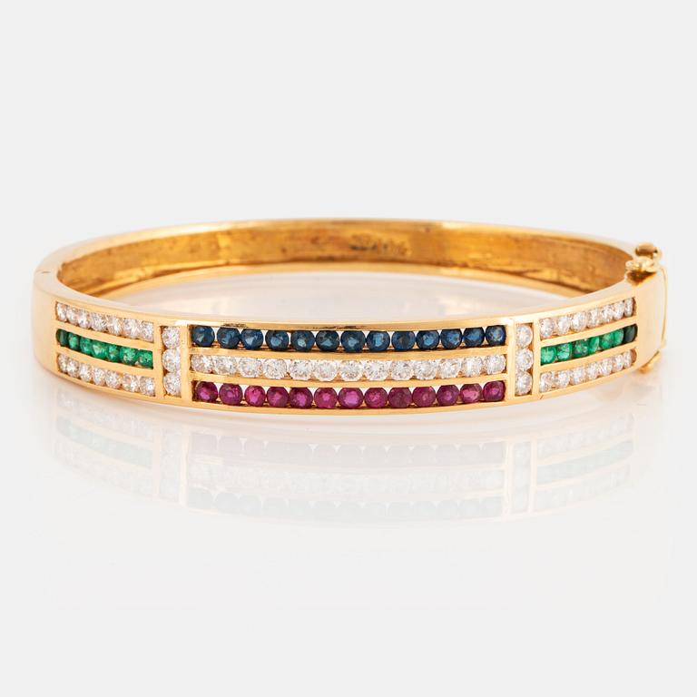 An 18K gold bangle set with round brilliant-cut diamonds, sapphires, emeralds and rubies.