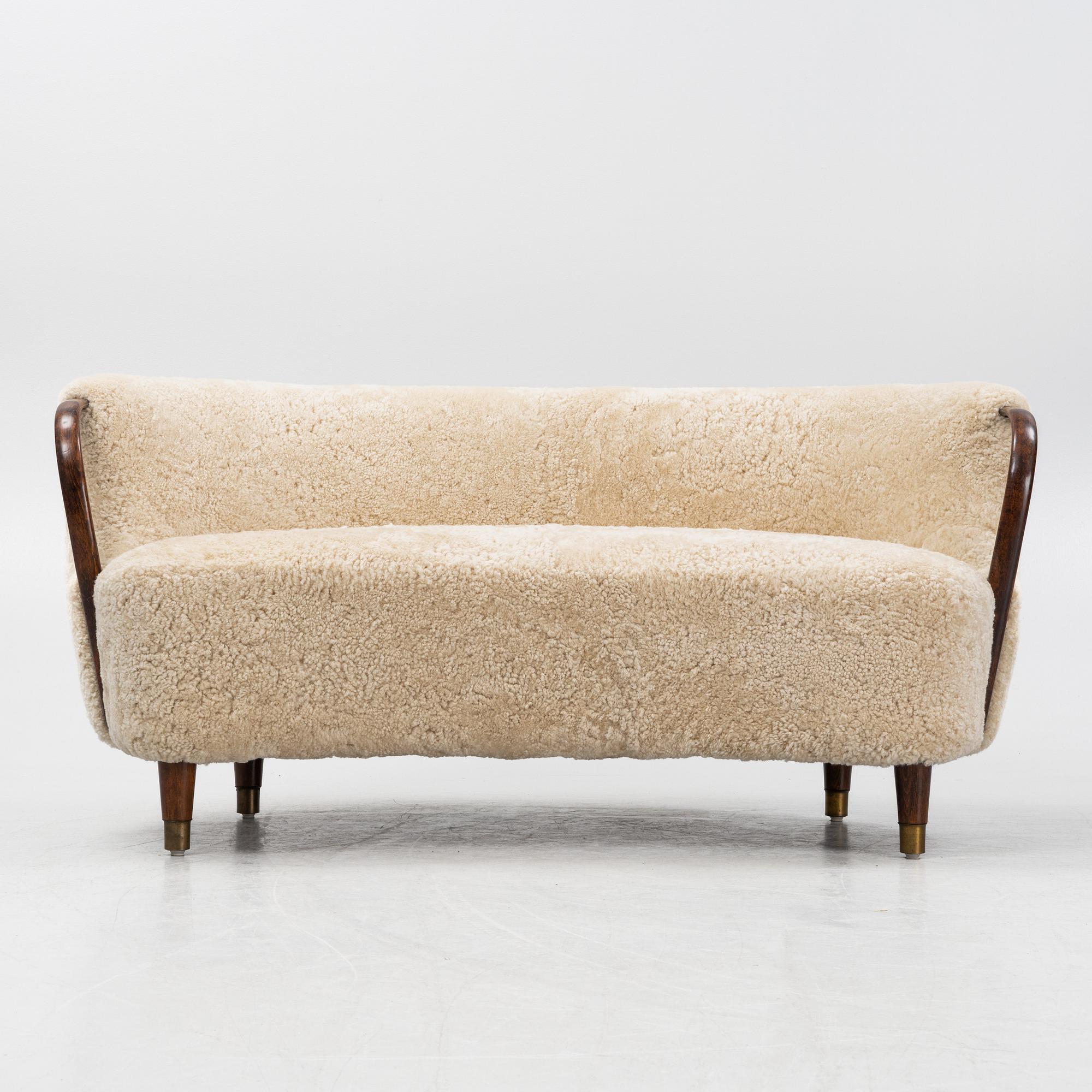 A curved sofa attributed to Viggo Boesen with new sheepskin upholstery and stained beech tree armrests.