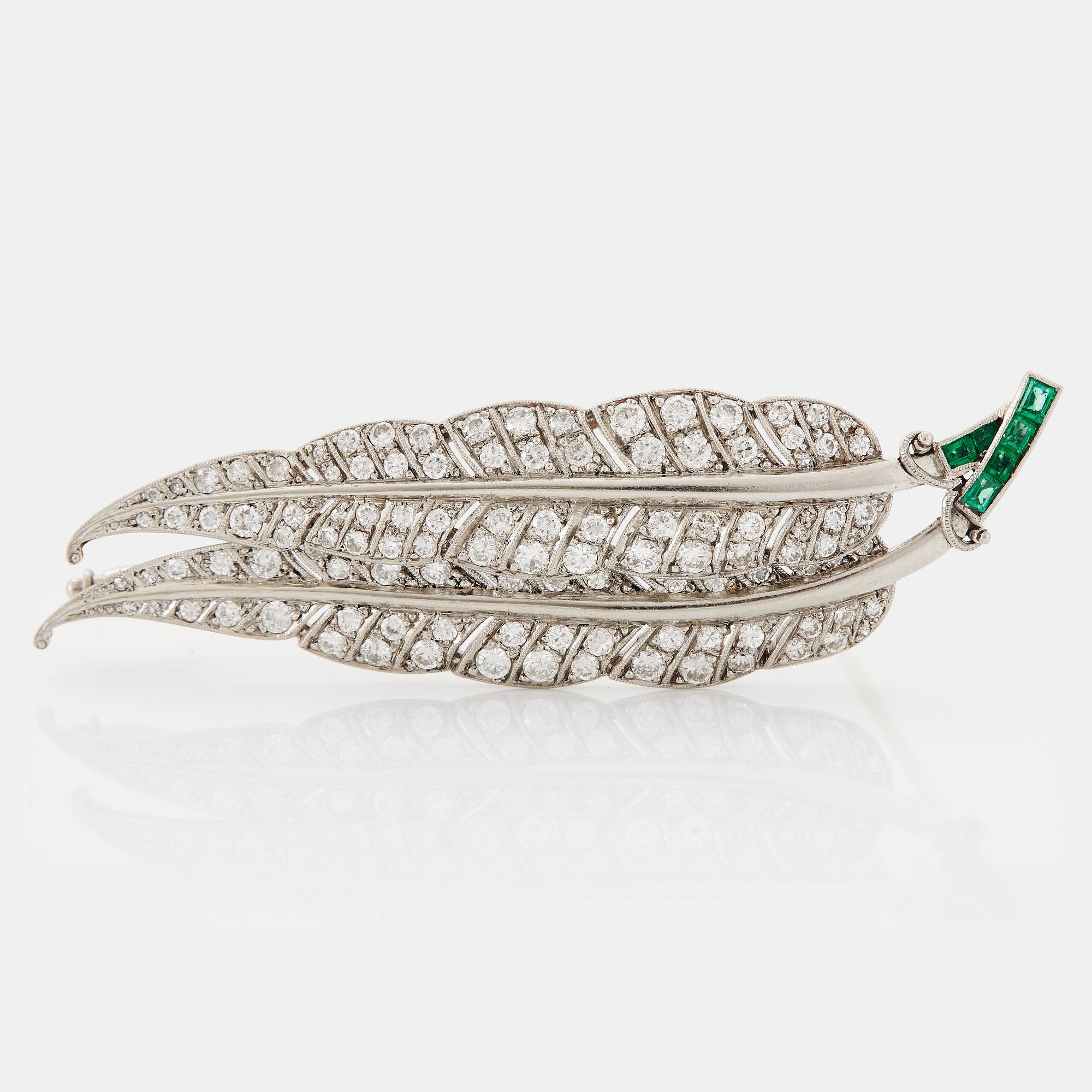 A platinum brooch set with round brilliant-cut diamonds and emeralds.