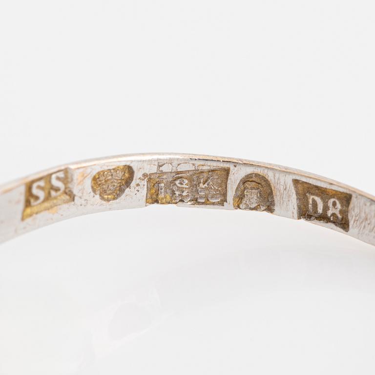 An 18K white gold ring set with a synthetic sapphire and round brilliant-cut diamonds.