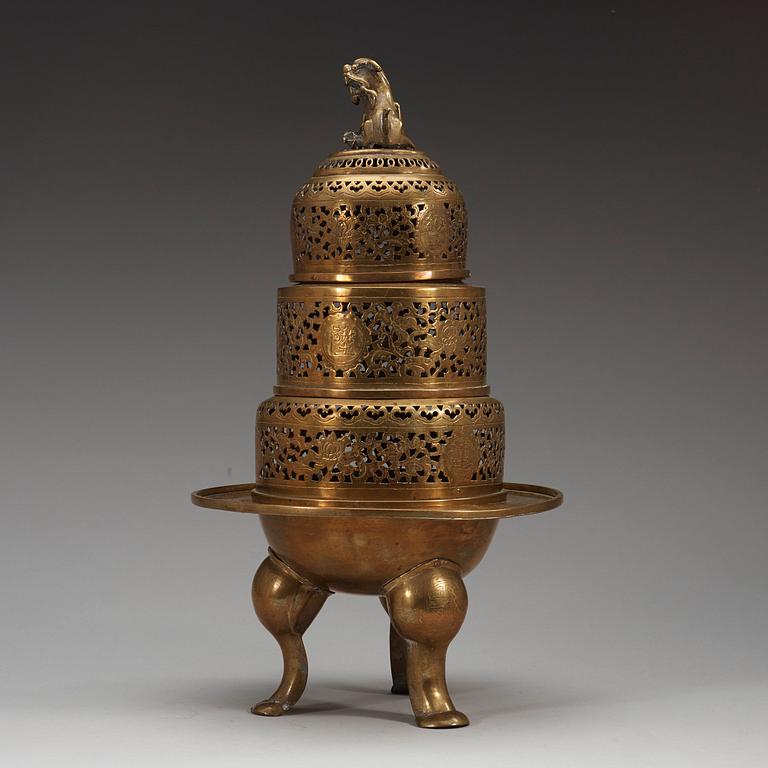 A four-part brass tripod censer, pierced sections with lotus scrolls and a fo-dog finial, late Qing dynasty (1644-1912).