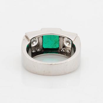 A platinum ring set with a step-cut emerald and round brilliant- and step-cut diamonds.