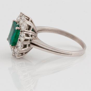 An 18K white gold ring set with a faceted emerald ca 1.15 cts and round brilliant-cut diamonds.