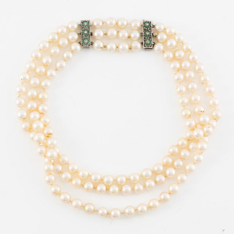 A three strand cultured pearl necklace, clasp in 18K gold with white stones and emeralds.
