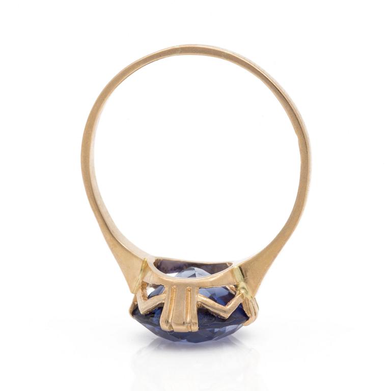 A ring set with a round, mixed-cut, synthetic sapphire.