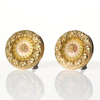 A pair of presumably English Empire repoussé gilt-brass and painted glass curtain tiebacks, early 19th century.