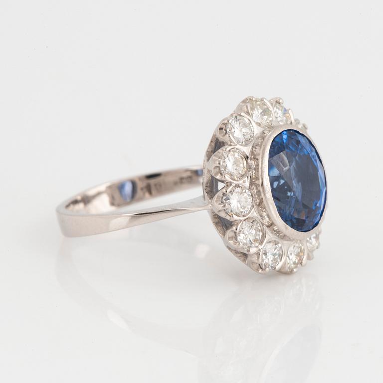 An 18K white gold ring set with a faceted sapphire and round brilliant-cut diamonds.