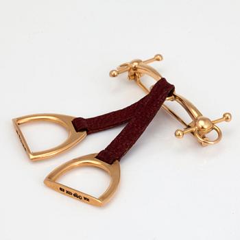 A stirrup and bridle brooch with leather details.