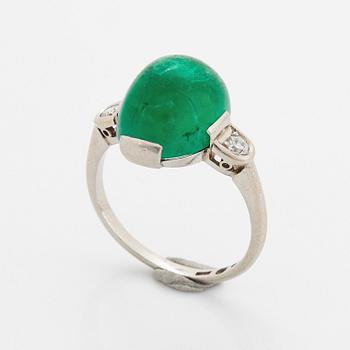 A platinum ring set with a cabochon-cut emerald and round brilliant-cut diamonds.