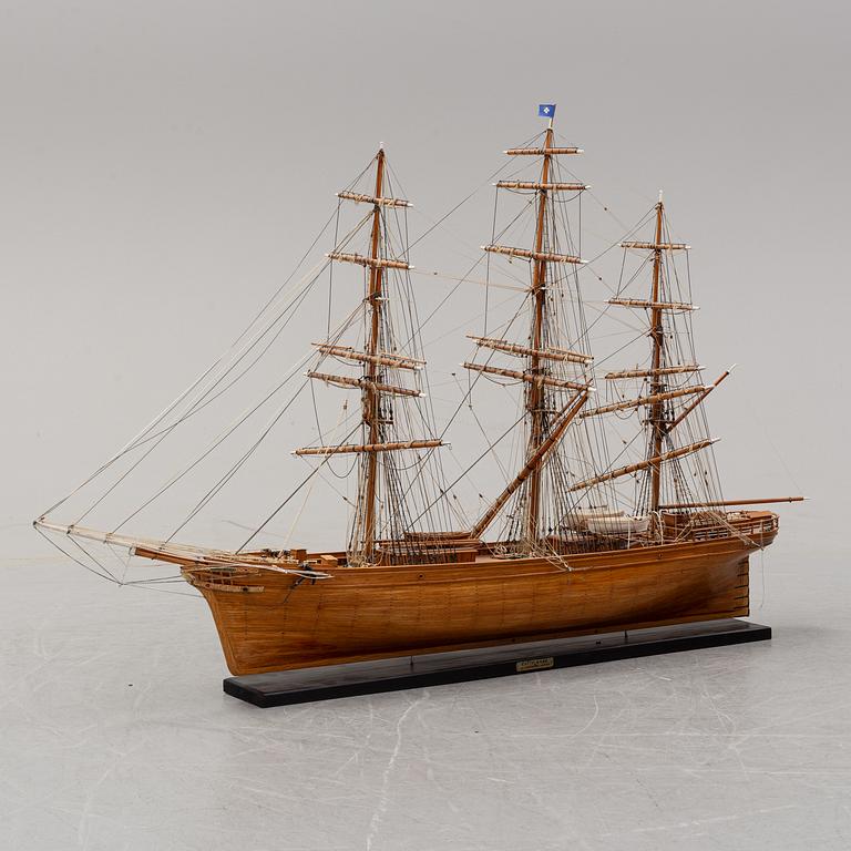 A wooden scale model of Cutty Sark on a painted wooden stand.