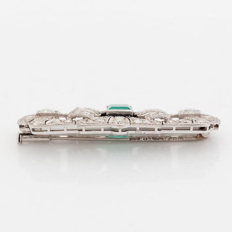 A platinum brooch set with a step-cut emerald and old- and eight-cut diamonds.