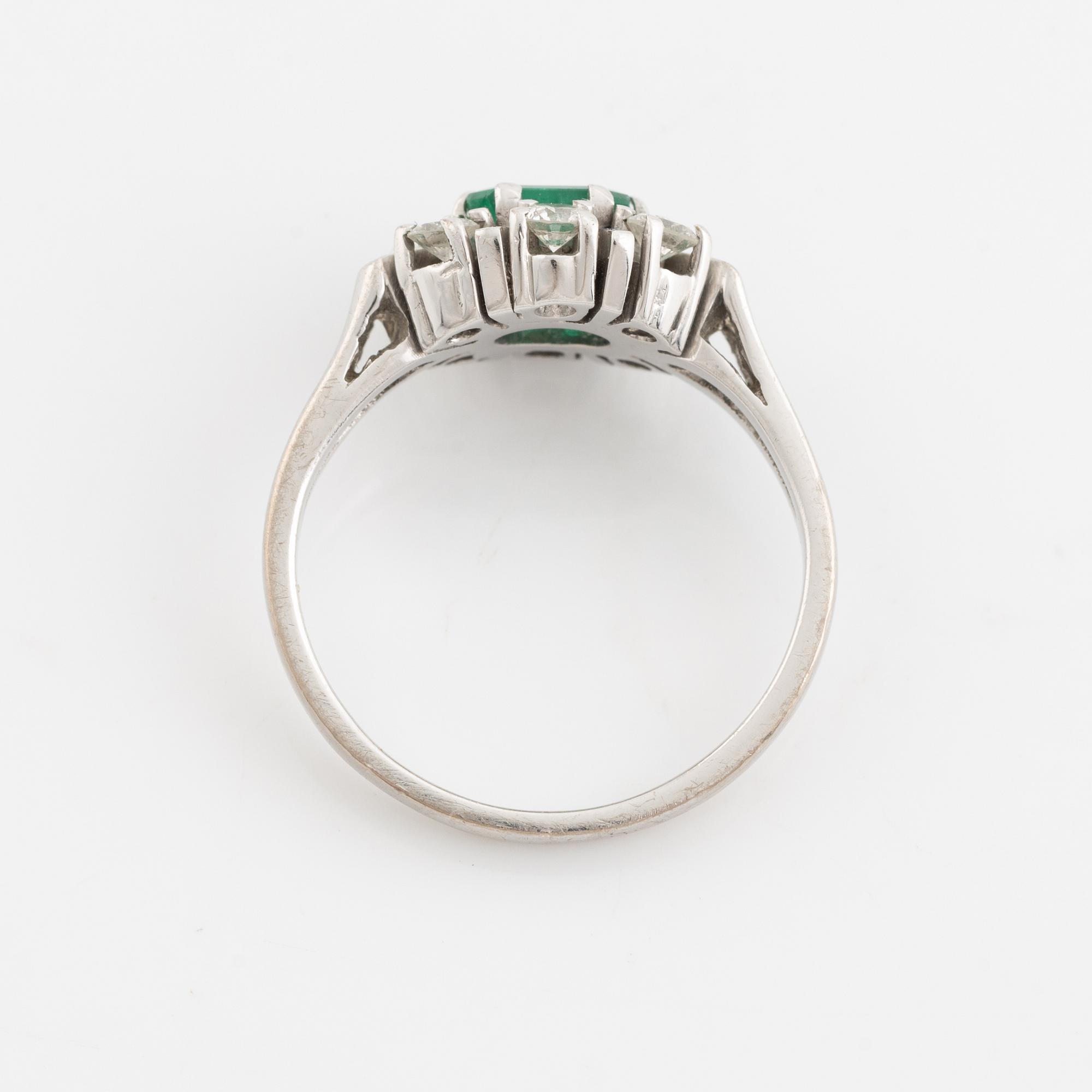 An 18K white gold ring set with a faceted emerald and round briliiant-cut diamonds.