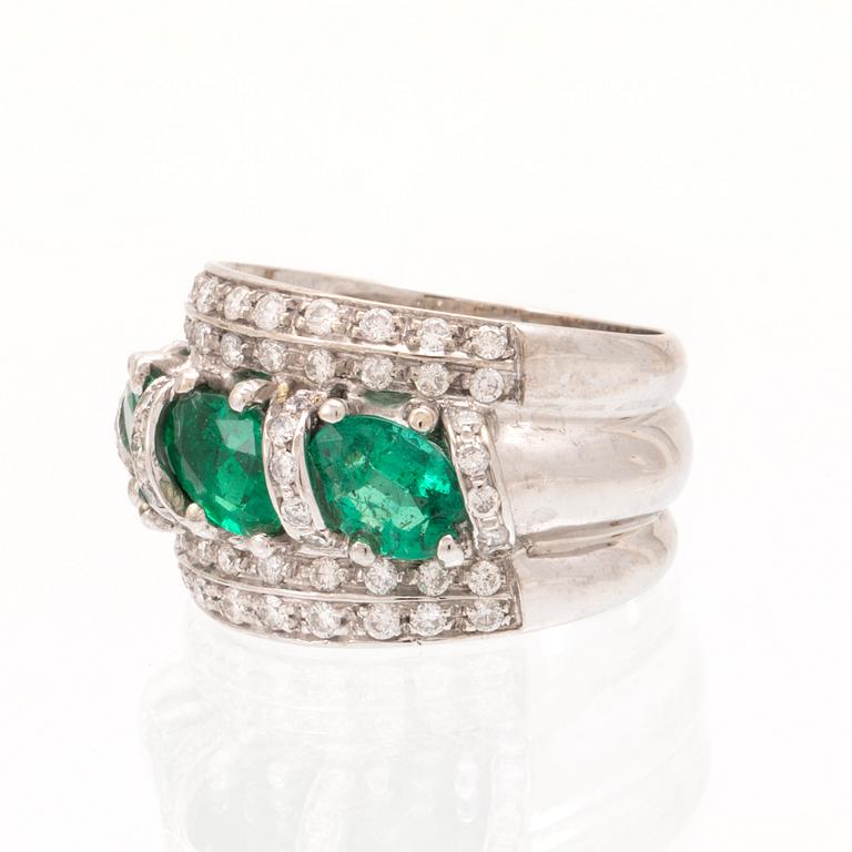 An 18K white gold ring set with oval cut emeralds and round brilliant cut diamonds.