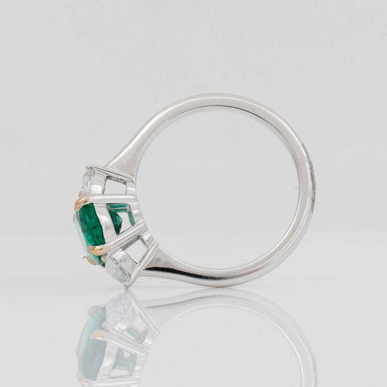 A 2.29ct oval-cut emerald ring. The emerald flanked by half moon shaped diamonds, total carat weight circa 0.81ct.