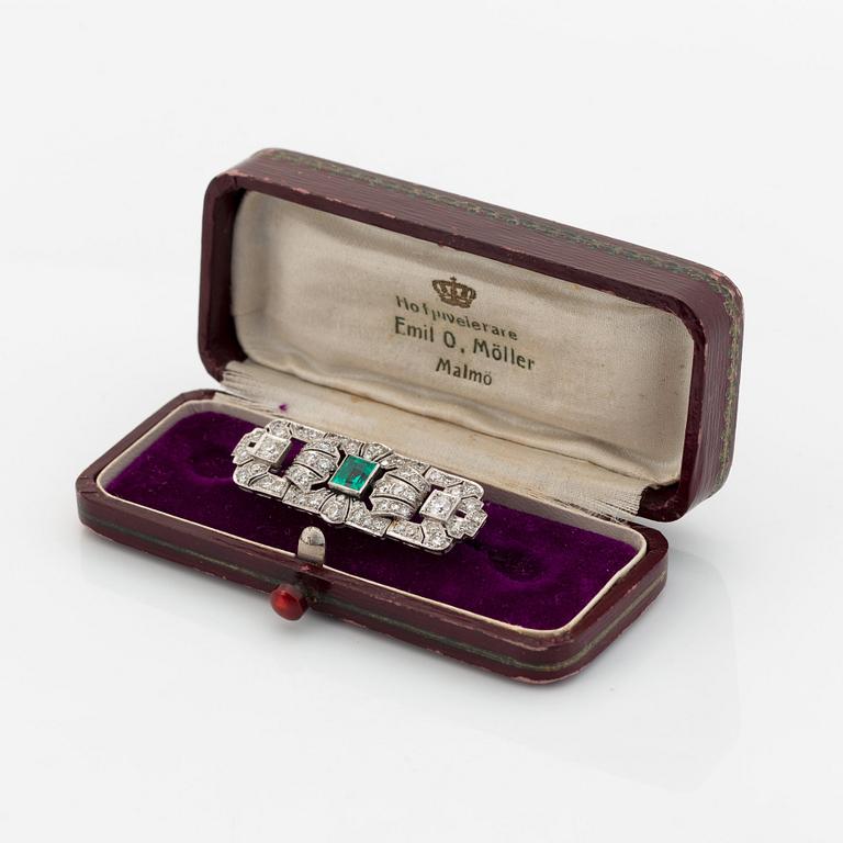 A platinum brooch set with a step-cut emerald and old- and eight-cut diamonds.