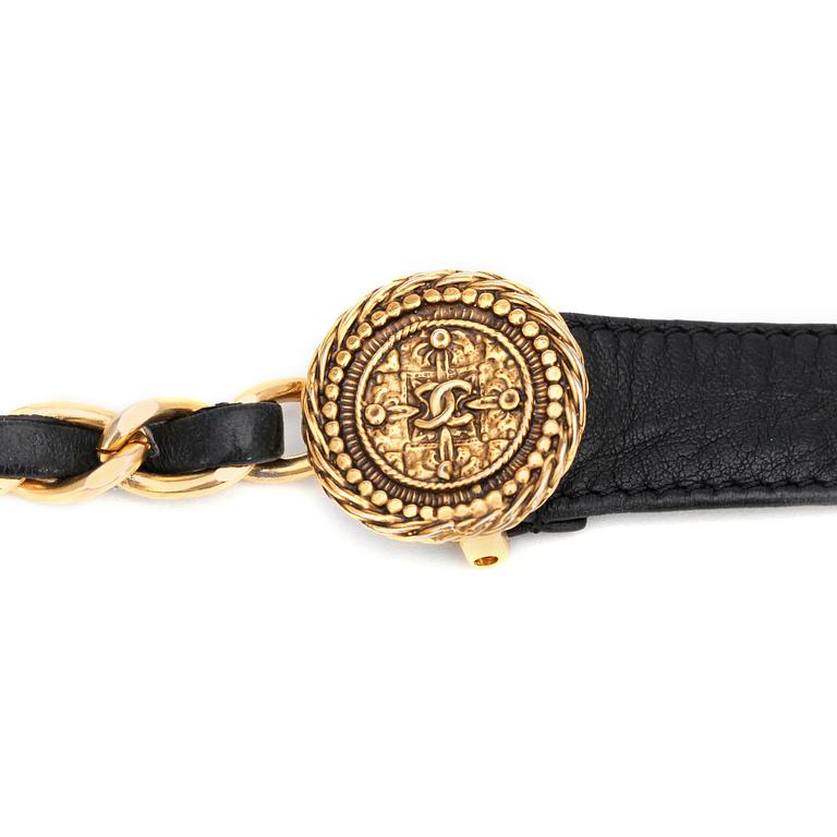 CHANEL, a black leather belt with gold colored metal chain.