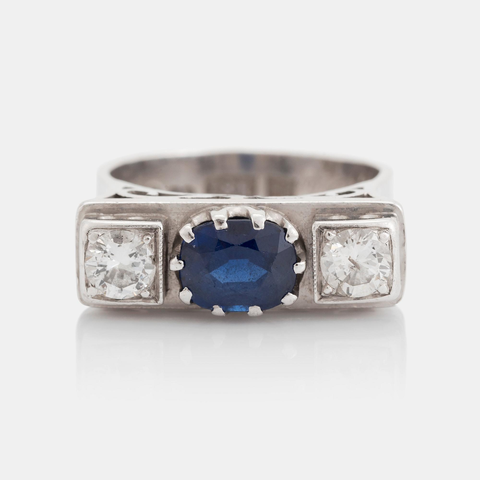 An 18K white gold ring set with a faceted sapphire, possibly synthetic, and round brilliant-cut diamonds.
