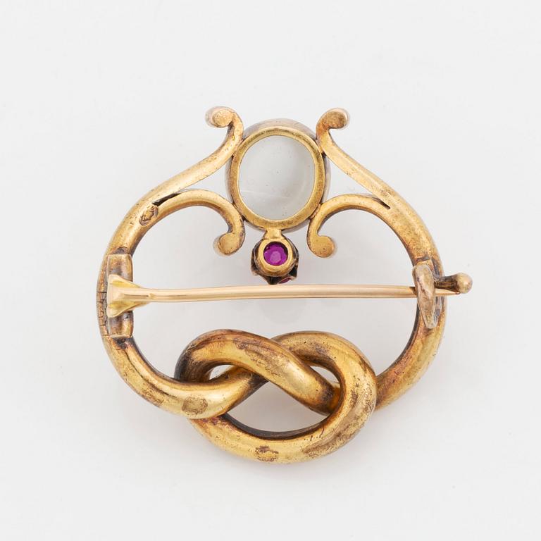 A 14K gold brooch set with a cabochon-cut moonstone and a pink sapphire.