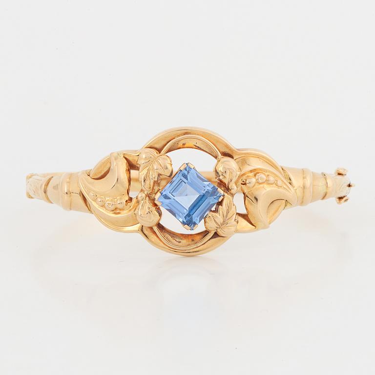 An 18K gold bangle set with a blue synthetic stone.