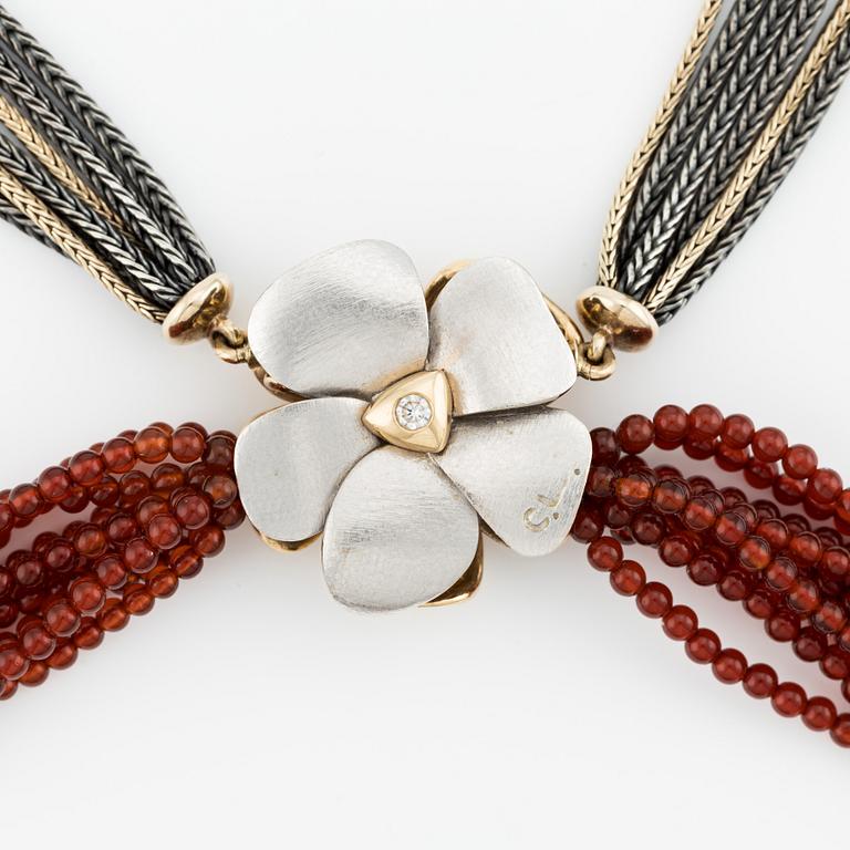Ole Lynggaard, clasp in the shape of a flower, 18K gold with diamonds and two colliers, one in silver and gold with red stone beads.