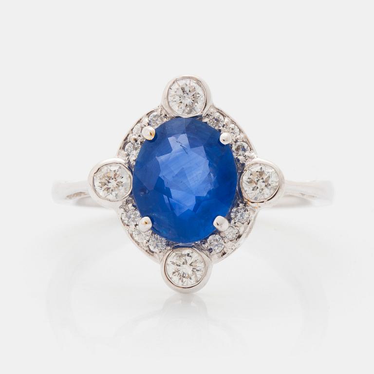 An 18K white gold ring set with a faceted sapphire and round brilliant-cut diamonds.