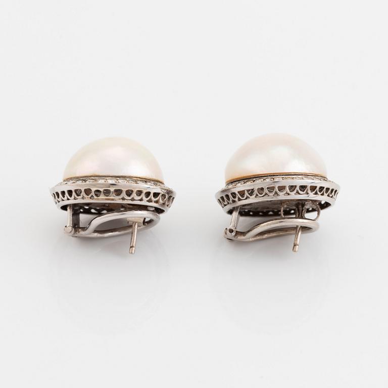 A pair of 18K white gold earrings set with cultured mabe pearls and round brilliant-cut diamonds.