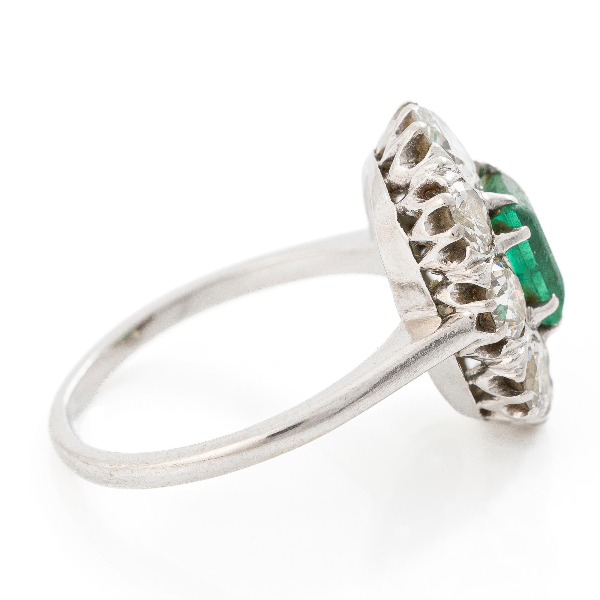 18K white gold ring set with a faceted emerald and round brilliant-cut diamonds.
